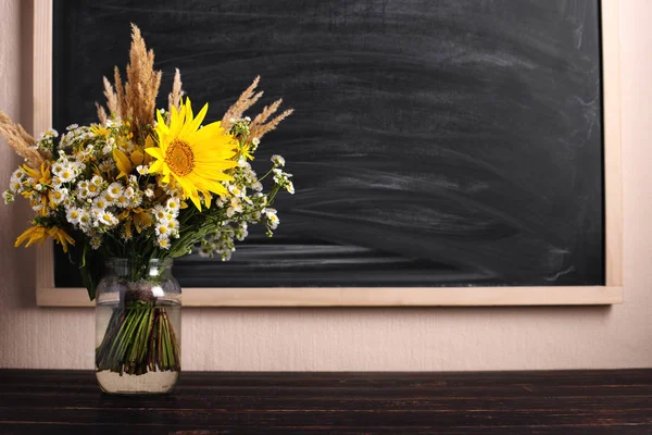 Teacher\'s day background. Black chalk board empty copy space and fresh wildflowers in vase. Holiday feminine poster.Spring greeting 8 march icon.