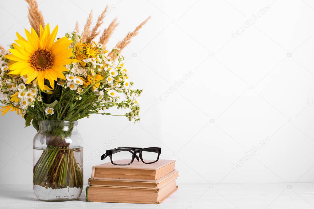 Summer bouquet of wildflowers in glass vase, old books on rustic background. Season design concept. Teachers day concept, back to school.