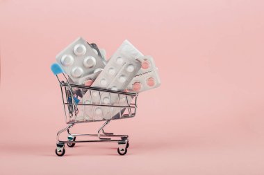 Alışveriş sepeti hapları pembe bir arka plan üzerinde yüklü. İlaç ve uyuşturucu satışı kavramı. Kopya alanı.