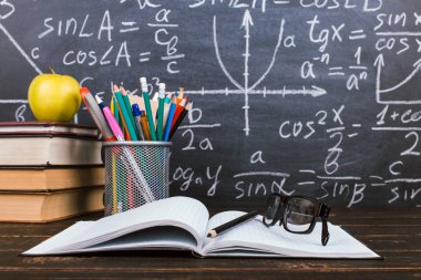 Defter, gözlük, elma ve formüller ile tebeşir arka plan üzerinde kalemler ile bir cam. Öğretmenler günü kavramı ve okula geri.