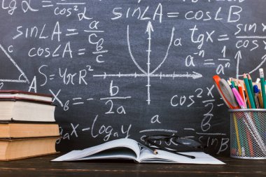 Kitaplar ve formüller ile bir tebeşir tahtası arka plan karşı, ahşap bir masa üzerinde kalem standı. Öğretmenler günü kavramı ve okula geri.