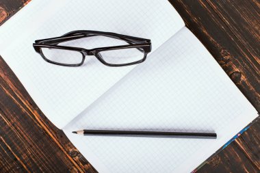 Tahta bir masanın üzerinde defter, kalem ve gözlük. Kopyalama alanı.