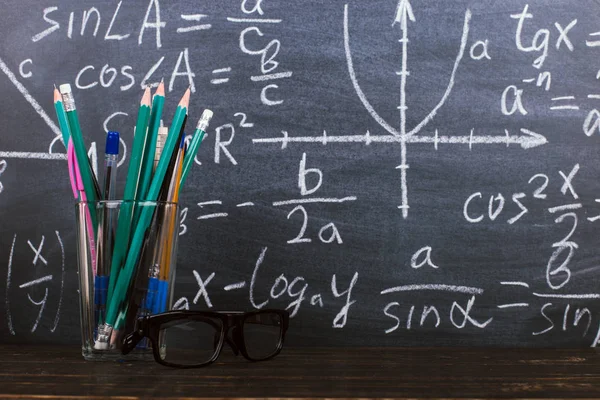 Gafas y un vaso con lápices sobre fondo de pizarra con fórmulas. Concepto del día del maestro y de vuelta a la escuela . — Foto de Stock