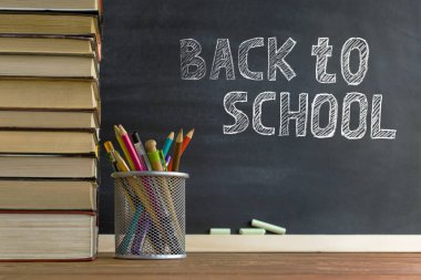 Ders kitapları ve okul malzemeleri bir masada, tebeşirle bir tahta arka plan karşı. Copyspase ile okul kavramı.