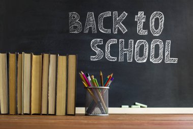 Ders kitapları ve okul malzemeleri bir masada, tebeşirle bir tahta arka plan karşı. Copyspase ile okul kavramı.