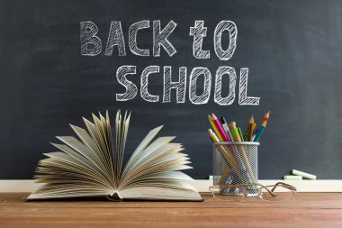 Gözlük öğretmen kitapları ve tebeşir ile bir tahta arka plan üzerinde, masada kalem ile bir stand. Öğretmenler günü kavramı. Kopyalama alanı.