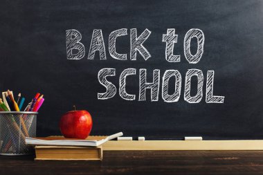 Yazma malzemeleri, bir kitap ve bir elma, metin için boş veya bir okul teması için bir arka plan ile Öğretmen masası. Kopyalama alanı.