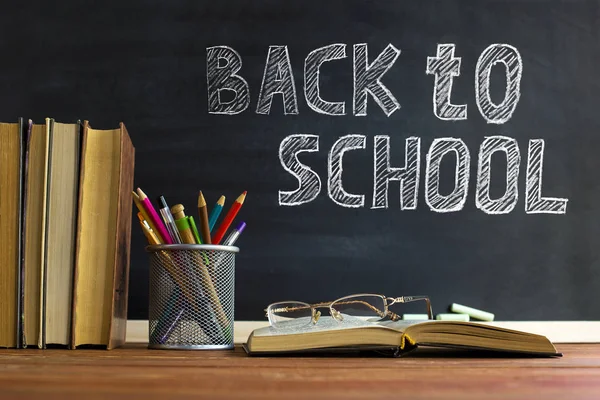 Gözlük öğretmen kitapları ve tebeşir ile bir tahta arka plan üzerinde, masada kalem ile bir stand. Öğretmenler günü kavramı. Kopyalama alanı.
