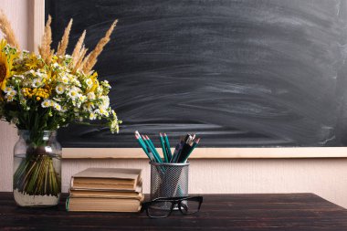 Gözlük öğretmen kitapları ve kır çiçekleri buket masada, tebeşir ile arka plan tahta üzerinde. Öğretmenler günü kavramı. Kopyalama alanı.