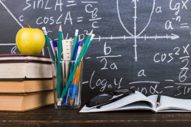 Defter, gözlük, elma ve formüller ile tebeşir arka plan üzerinde kalemler ile bir cam. Öğretmenler günü kavramı ve okula geri.