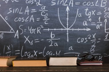 Formülleri ile bir tebeşir tahtası arka plan karşı ahşap bir masa üzerinde Kitaplar. Öğretmenler günü kavramı ve okula geri.