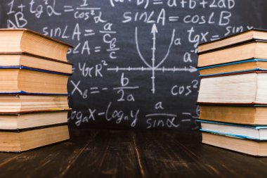 Formülleri ile bir tebeşir tahtası arka plan karşı ahşap bir masa üzerinde Kitaplar. Öğretmenler günü kavramı ve okula geri.