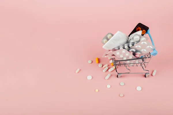 Winkelwagen geladen met pillen op een roze achtergrond. De concep — Stockfoto