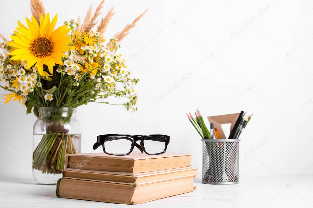 Summer bouquet of wildflowers in glass vase, old books on rustic background. Season design concept. Teachers day concept, back to school.