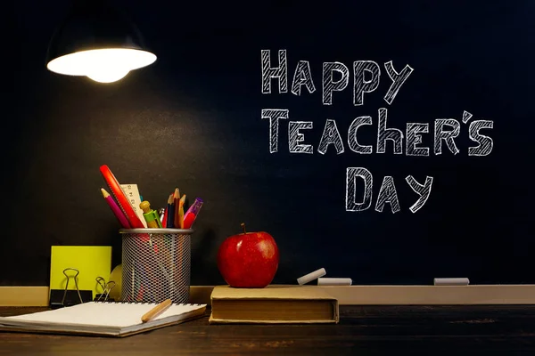 The teacher\'s desk or a worker, on which the writing materials lie, a book and an apple, in the evening under the lamp. Blank for text or background for a school theme. Copy space.
