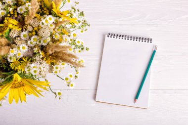 Beyaz bir masaüzerinde çiçek, defter ve kalem buketi. Kopyalama alanı.