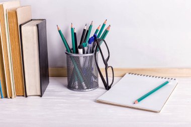 Beyaz bir tahtanın arka planına karşı masanın üzerinde kitaplar, işaretler, defter, kalem ve gözlükler. Kopyalama alanı.