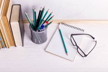 Beyaz bir tahtanın arka planına karşı masanın üzerinde kitaplar, işaretler, defter, kalem ve gözlükler. Kopyalama alanı.