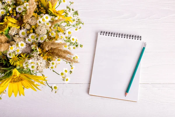 Boeket van bloemen, notebook en potlood op een witte tafel. Ruimte kopiëren. — Stockfoto