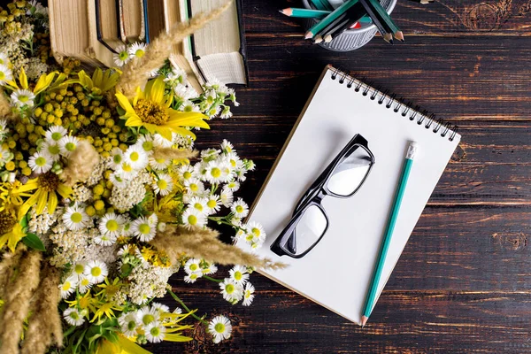 Libros, vasos, marcadores y un ramo de flores en un jarrón sobre fondo de pizarra blanca. Concepto para el día del profesorado y primer septiembre. Copiar espacio . — Foto de Stock