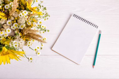 Beyaz bir masaüzerinde çiçek, defter ve kalem buketi. Kopyalama alanı.
