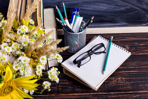 Libros, vasos, marcadores y un ramo de flores en un jarrón sobre fondo de pizarra blanca. Concepto para el día del profesorado y primer septiembre. Copiar espacio . — Foto de Stock