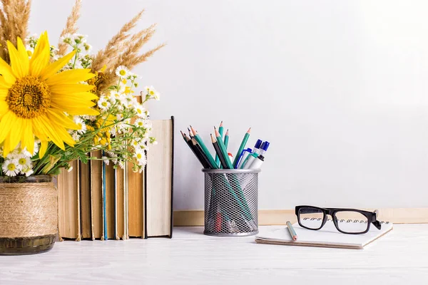 Livros, copos, marcadores e um buquê de flores em um vaso no fundo do tabuleiro branco. Conceito para professores dia e primeiro de setembro. Espaço de cópia . — Fotografia de Stock