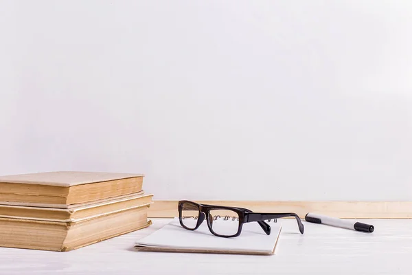 Boeken en brillen op tafel tegen de achtergrond van een wit bord. Ruimte kopiëren. — Stockfoto