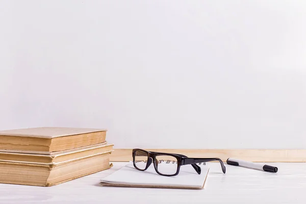 Libri e bicchieri sul tavolo sullo sfondo di una lavagna bianca. Copia spazio . — Foto Stock