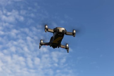 Bir drone, video çekimi için bir kamera ile bir quadrocopter, bulutlar ile mavi bir gökyüzüne karşı uçar.