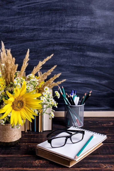 Libros, vasos, marcadores y un ramo de flores en un jarrón sobre fondo de pizarra blanca. Concepto para el día del profesorado y primer septiembre. Copiar espacio . — Foto de Stock