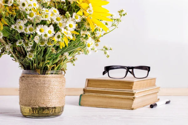 Livros, copos, marcadores e um buquê de flores em um vaso no fundo do tabuleiro branco. Conceito para professores dia e primeiro de setembro. Espaço de cópia . — Fotografia de Stock