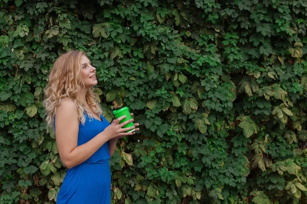 Jonge mooie meid op een achtergrond van een muur van wilde druiven die koffie drinken. Ruimte kopiëren. — Stockfoto