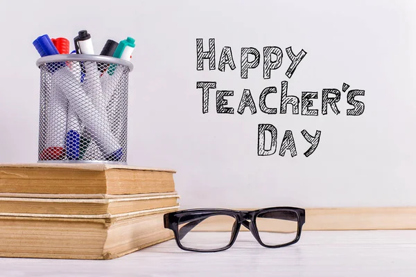 O marcador de inscrição em um quadro branco, Happy Teacher 's Day. Uma mesa com livros, óculos e atributos para escrever . — Fotografia de Stock