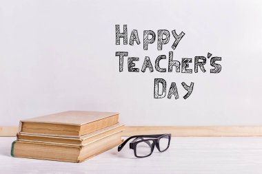 Beyaz tahtadaki yazıt işareti, Mutlu Öğretmenler Günü. Kitap ve gözlüklü bir masa.