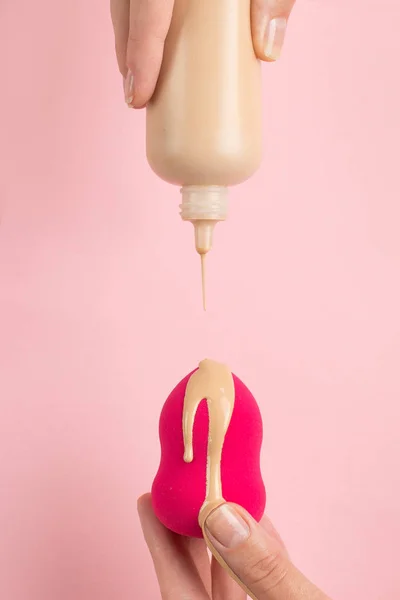 A mão da menina segura o liquidificador de beleza na fundação, corretor no fundo rosa. Maquiagem conceito artista, espaço de cópia . — Fotografia de Stock