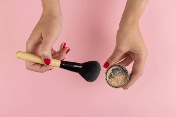 Girl's hands hold powder and makeup brush on a pink background, copy space. — Stock Photo, Image