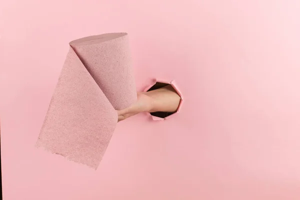 Frau Hand hält Toilettenpapier aus einem Loch in einem rosa Hintergrund. Konzept, Kopierraum. — Stockfoto