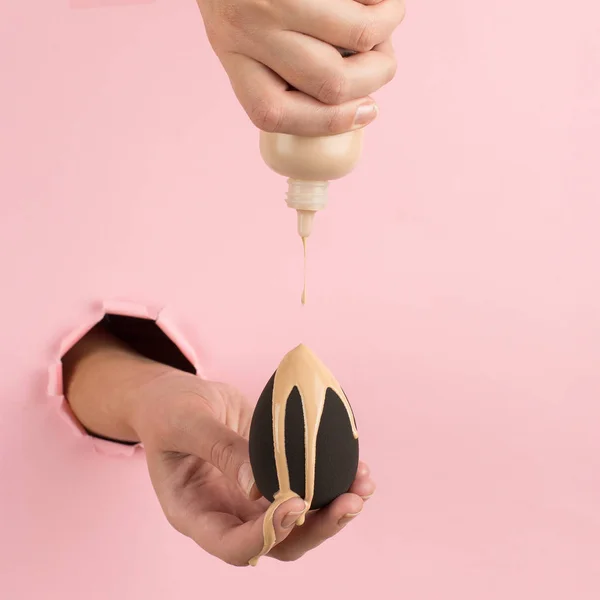 Kız el temel bir güzellik blender tutar, pembe bir arka plan bir delik kapatıcı. Makyaj sanatçısı kavramı, kopyalama alanı.
