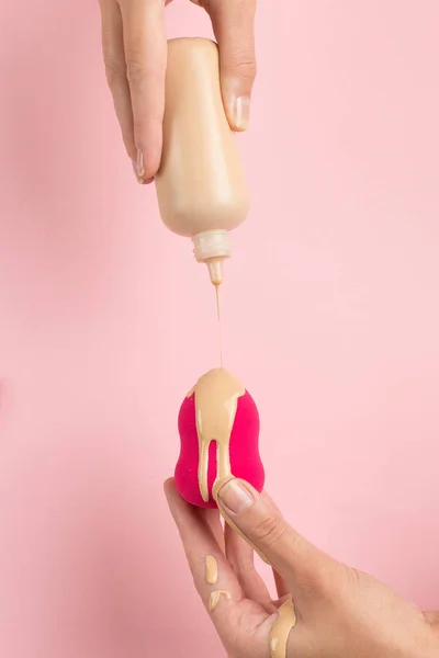 La mano de la muchacha sostiene la licuadora de belleza en la fundación, corrector sobre fondo rosa. Maquillaje artista concepto, espacio de copia . —  Fotos de Stock