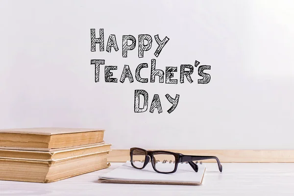 O marcador de inscrição em um quadro branco, Happy Teacher 's Day. Uma mesa com livros e óculos . — Fotografia de Stock