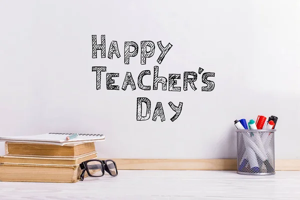 O marcador de inscrição em um quadro branco, Happy Teacher 's Day. Uma mesa com livros, óculos e atributos para escrever . — Fotografia de Stock