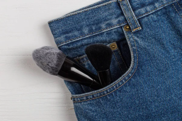 Large makeup brushes in a pocket of blue jeans. Concept, commercial work of a makeup artist, for printing business cards and brochures.
