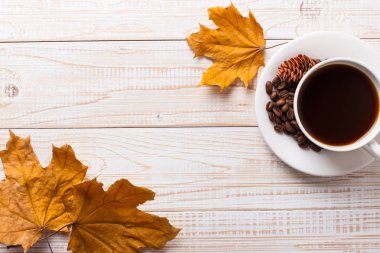 Dağınık kahve çekirdekleri ile kahve fincan, ahşap bir masada kuru sarı yaprakları. Sonbahar sabah ruh hali, kopya alanı.