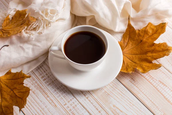 흰색 스카프, 커피 한 잔, 나무 테이블에 마른 노란색 잎. 가을 무드·카피 스페이스. — 스톡 사진
