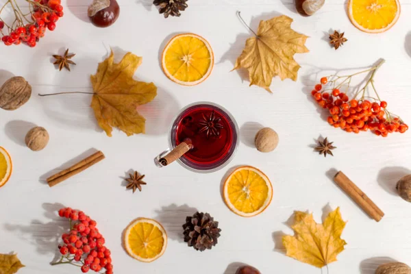 Una taza de vino caliente con especias, hojas secas y naranjas sobre la mesa. El estado de ánimo de otoño, un método para mantener el calor en el frío, la luz de la mañana, la puesta plana . —  Fotos de Stock