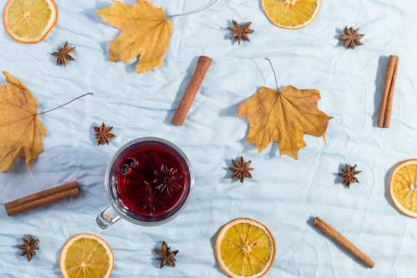 Una taza de vino caliente con especias, hojas secas y naranjas sobre la mesa. Humor de otoño, método para mantener el calor en frío, espacio de copia, luz de la mañana, acostado plano . —  Fotos de Stock