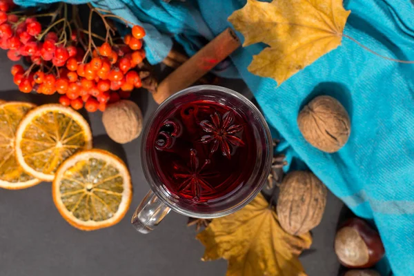 Filiżanka grzane wino z przyprawami, szalik, suche liście i pomarańcze na kamiennym stole. Jesienny nastrój, Metoda utrzymywania ciepła w zimnej. — Zdjęcie stockowe