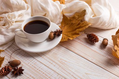 Beyaz eşarp, bir fincan kahve ve tahta bir masa üzerinde kuru sarı yaprakları. Sonbahar ruh hali, kopya alanı.
