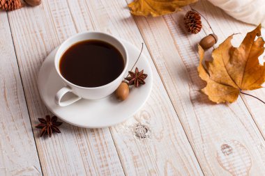 Beyaz eşarp, bir fincan kahve ve tahta bir masa üzerinde kuru sarı yaprakları. Sonbahar ruh hali, kopya alanı.